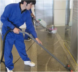 清掃会社の職員がマンションホールの床を床洗浄機と掃除機で清掃している写真