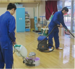 清掃会社の職員が学校の茶色い床を床洗浄機で清掃している写真